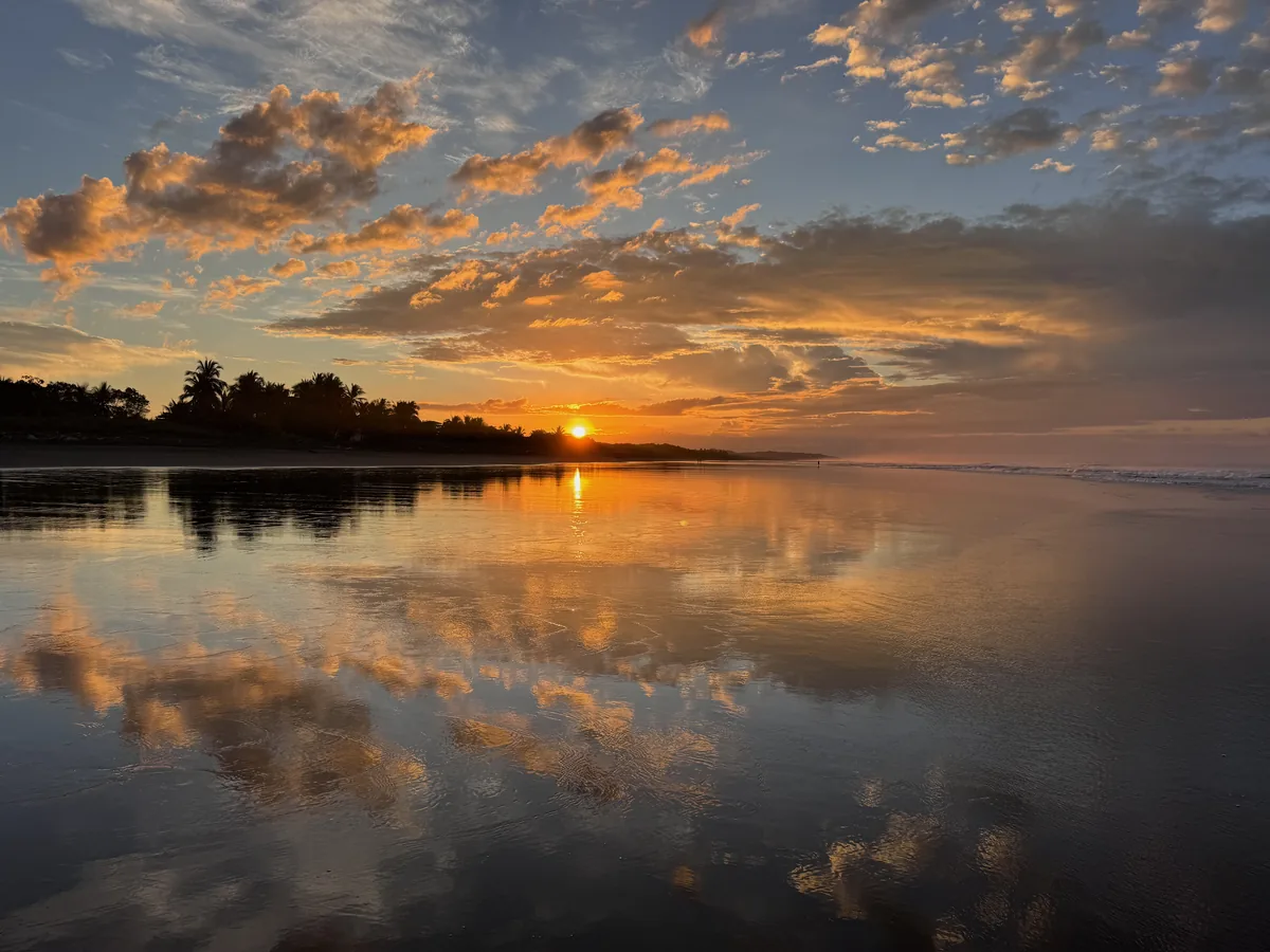 Golden sunrise reflected across the wet black sand on Costa Rica's Central Pacific coast